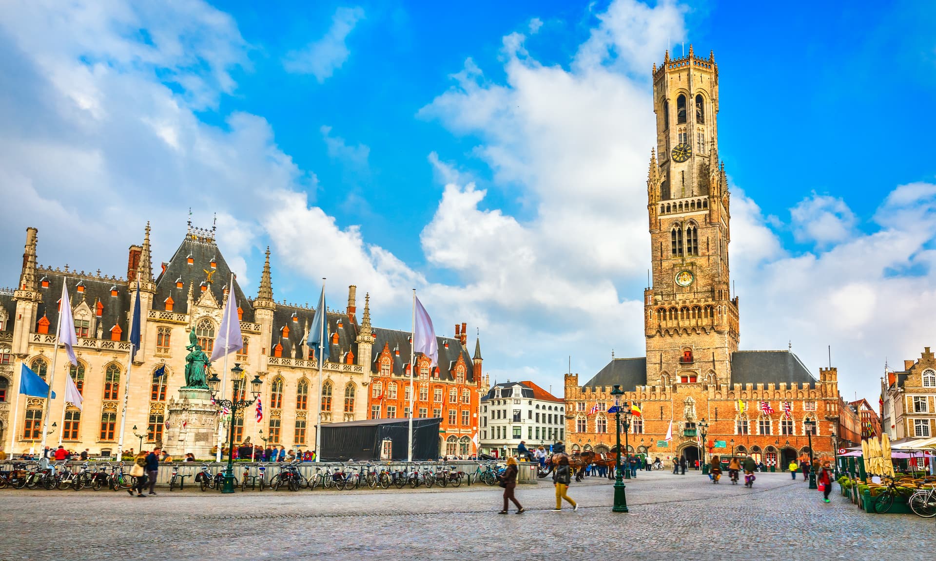 Historic Bruges Market Square with Belfry tower, historic buildings, and bicycles parked.