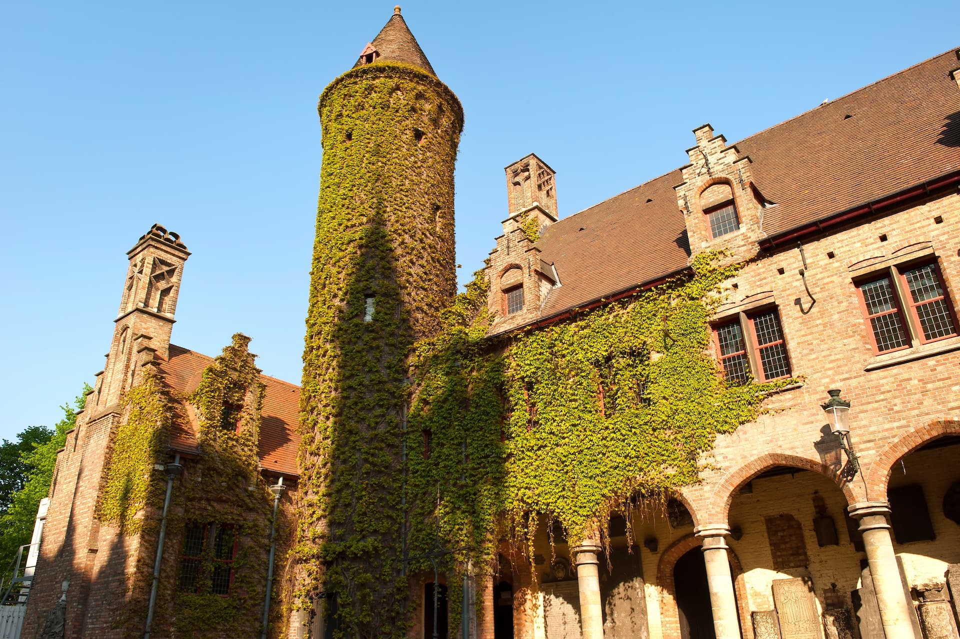 Historic brick building with ivy-covered tower and arched loggia under clear blue sky.