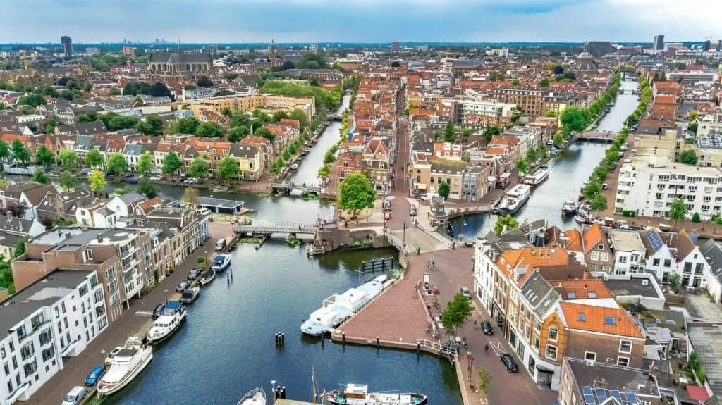 Aerial view of Leiden city canals lined with historic buildings and moored boats under a cloudy sky.
