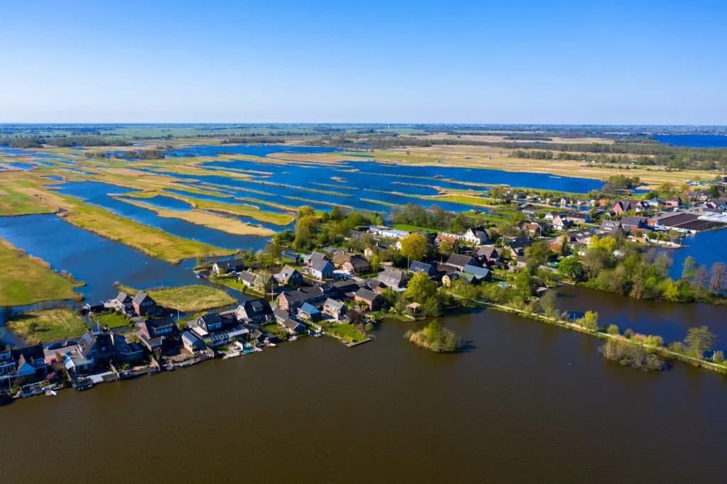 Aerial view of Nieuwkoop village surrounded by polders and dark water under a clear blue sky.