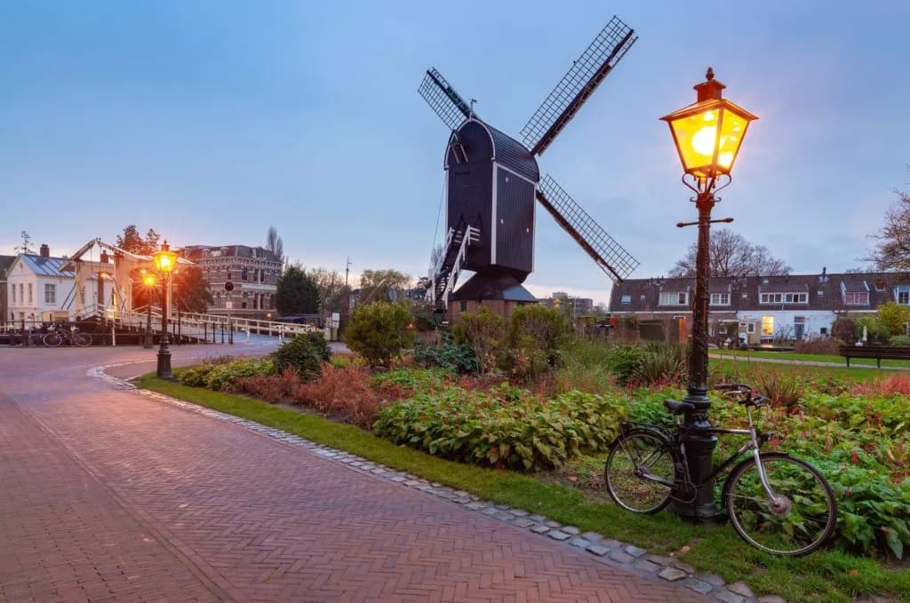 Black windmill near a lit streetlamp and bicycle on a brick path in Leiden.