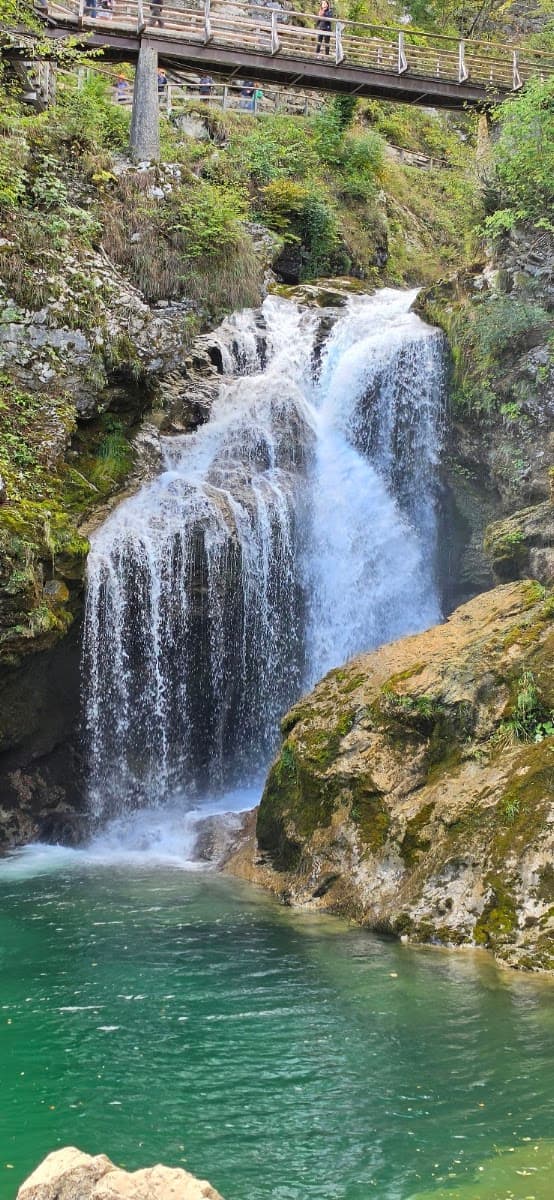 Waterfall cascading into a turquoise pool with a wooden footbridge above