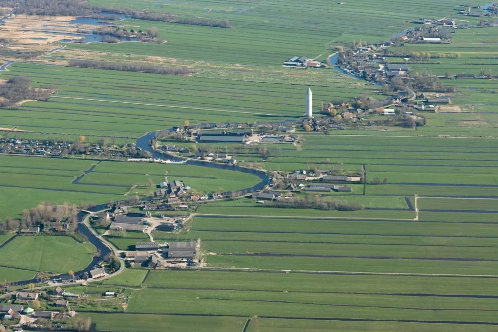 Aerial view of Nieuwkoop with a winding river, green polder fields, and a tall water tower.